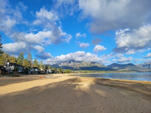 Een strand met een helder uitzicht op bergen in de verte, een zandvlakte en enkele gebouwen nabij het water.