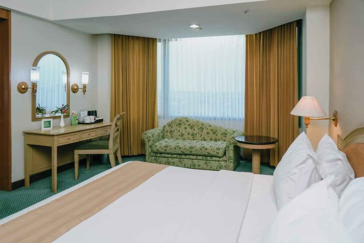 A hotel room with a bed, a desk, a chair, a small table, a lamp, and a large window with curtains.