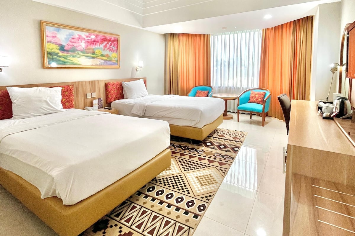 A hotel room with two beds, a desk, a chair, and a large window with curtains.