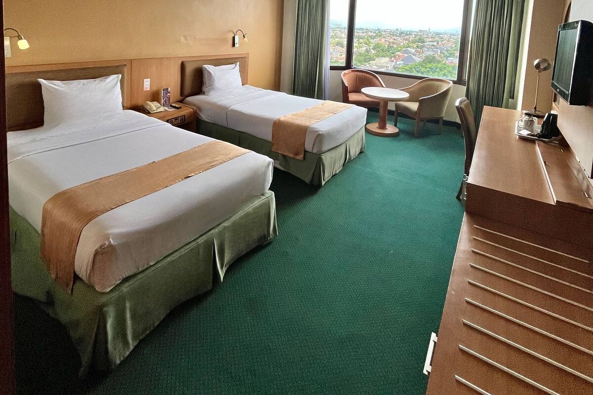 A hotel room with two beds, a desk, a chair, and a view of the city.