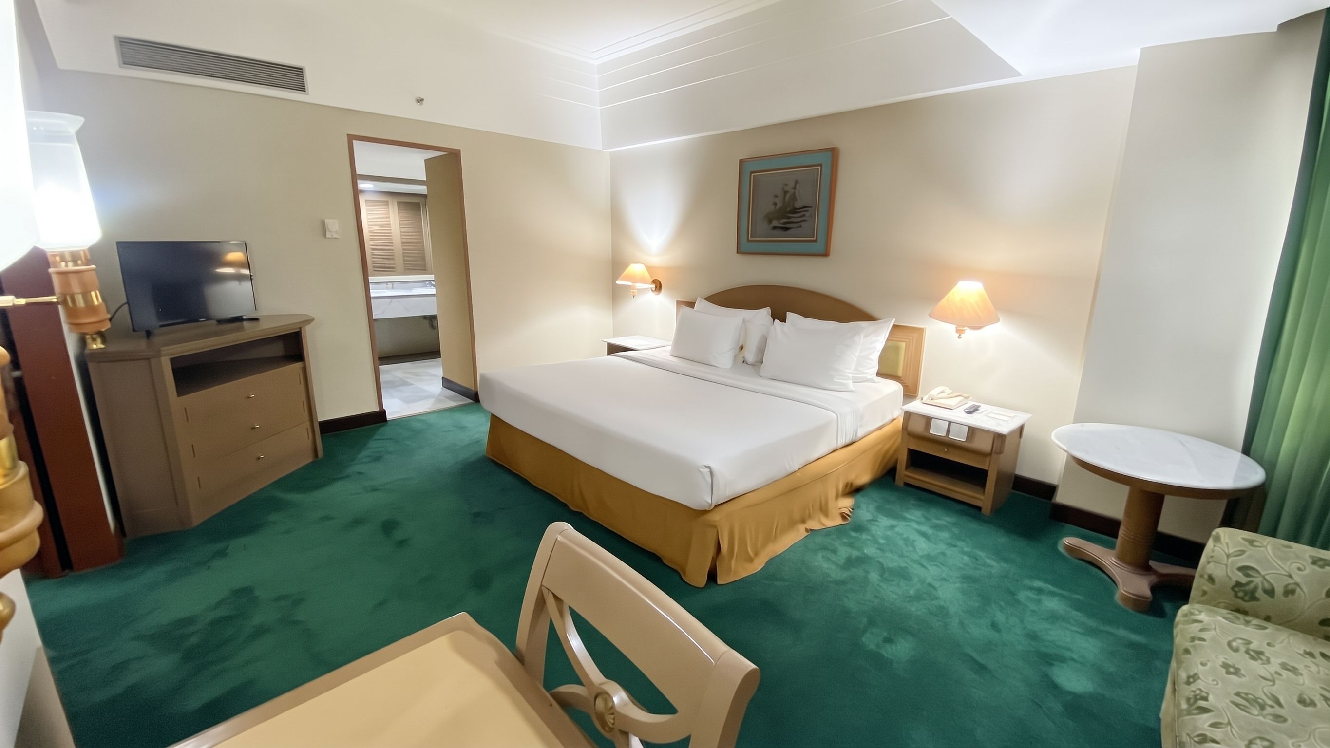 A hotel room with a bed, bedside tables, a desk, a chair, and a television.