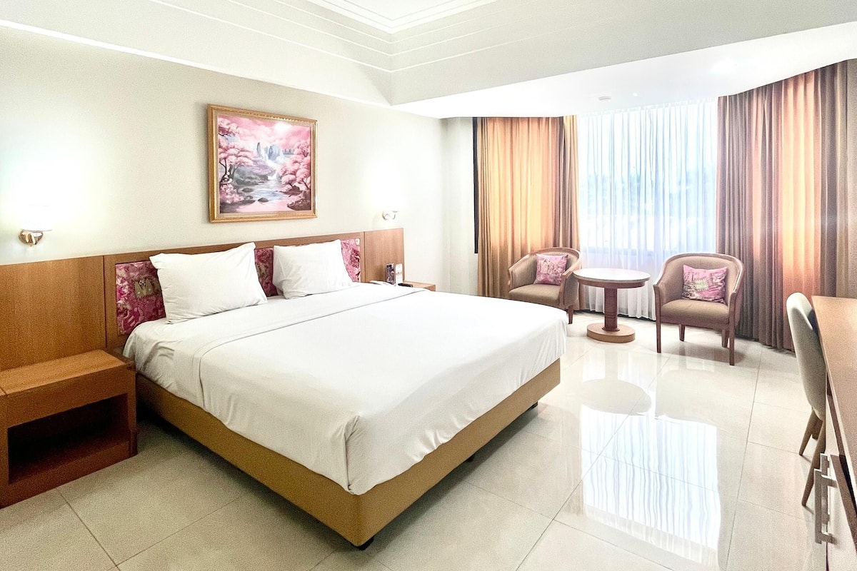 A hotel room with a large bed, a desk, a chair, and a small table.