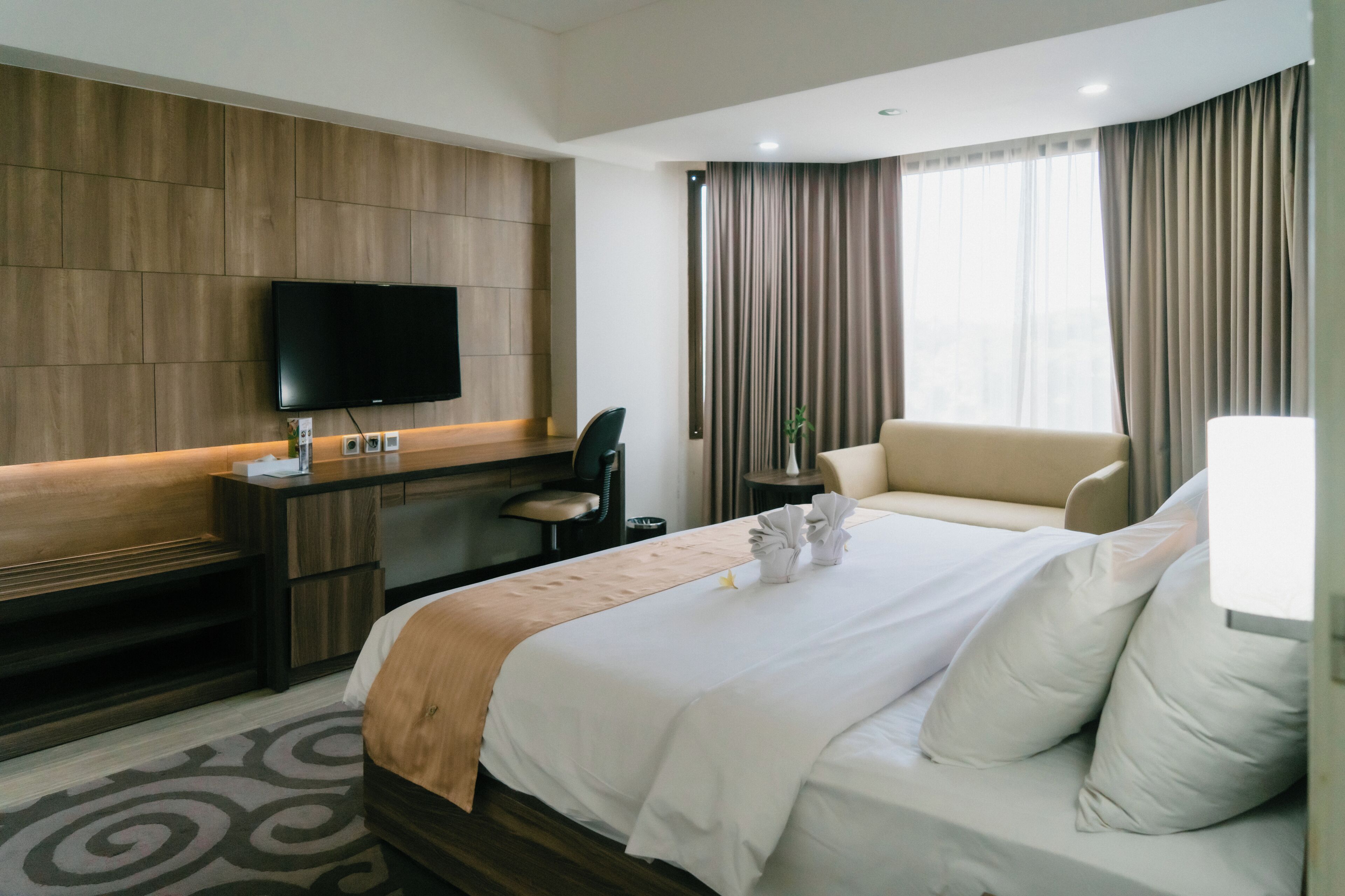 Une chambre d’hôtel équipée d’un lit, d’un bureau, d’une chaise, d’une télévision et d’une fenêtre avec des rideaux.