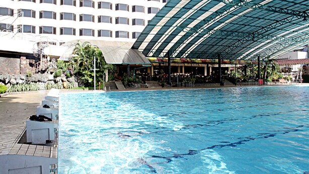 Piscina com divisórias de pista, rodeada por espreguiçadeiras e uma área de estar coberta.