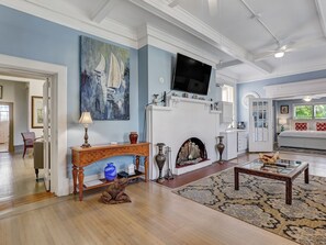 Un salon spacieux doté d’une cheminée, d’un téléviseur fixé au-dessus et d’un grand tableau accroché au mur.