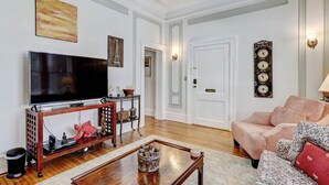 Una sala de estar con un televisor de pantalla plana, una mesa de centro de madera, un sofá estampado y un elemento decorativo en la pared.