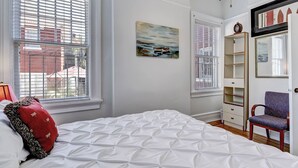 Un dormitorio con una cama grande, una silla, una estantería y un cuadro en la pared.