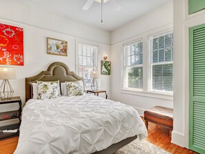 Ein Schlafzimmer mit Bett, Nachttischen, einem Fenster mit Jalousien und Bildern an den Wänden.