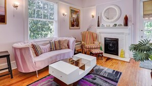 Una sala de estar con un sofá rosa, sillones a rayas, una mesa de centro blanca y una chimenea.