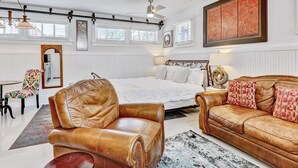 Une chambre spacieuse avec un grand lit, des fauteuils en cuir, un canapé en cuir marron et un grand tableau abstrait accroché au mur.