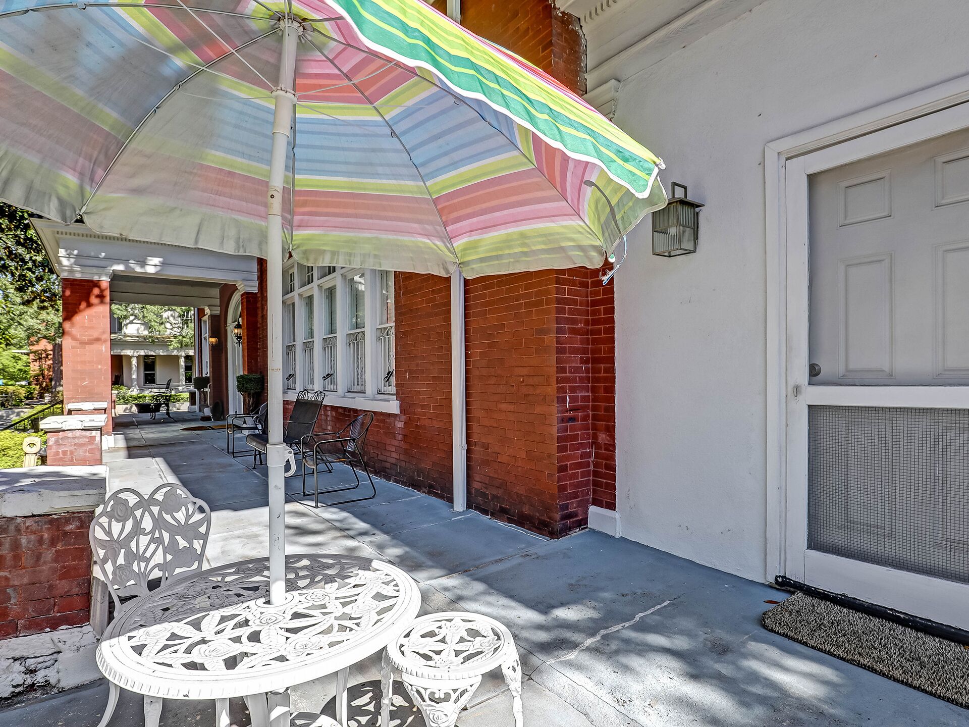 Un patio abrité avec un parasol à rayures, des chaises en métal blanc et une table.