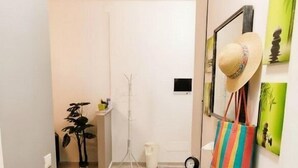 A hallway with a wooden bench, a striped bag, a hat, and a small table with books and a clock. - Apartment with A/C close to beaches | Ap26 (Imperia)