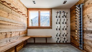 Un refugio de esquí con paredes de madera, un banco, una ventana con vistas a la montaña y un esquiador con sus esquíes.