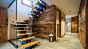 Una escalera moderna con barandillas de vidrio y escalones de madera, que lleva a una habitación con paredes de madera y suelo de baldosas.