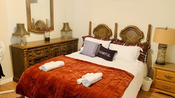 A neatly made bed with a red quilt, two pillows, and two rolled towels.