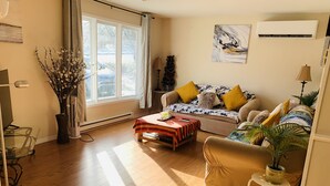 A living room with a sofa, a coffee table, a lamp, a plant, and a window with a view of trees.