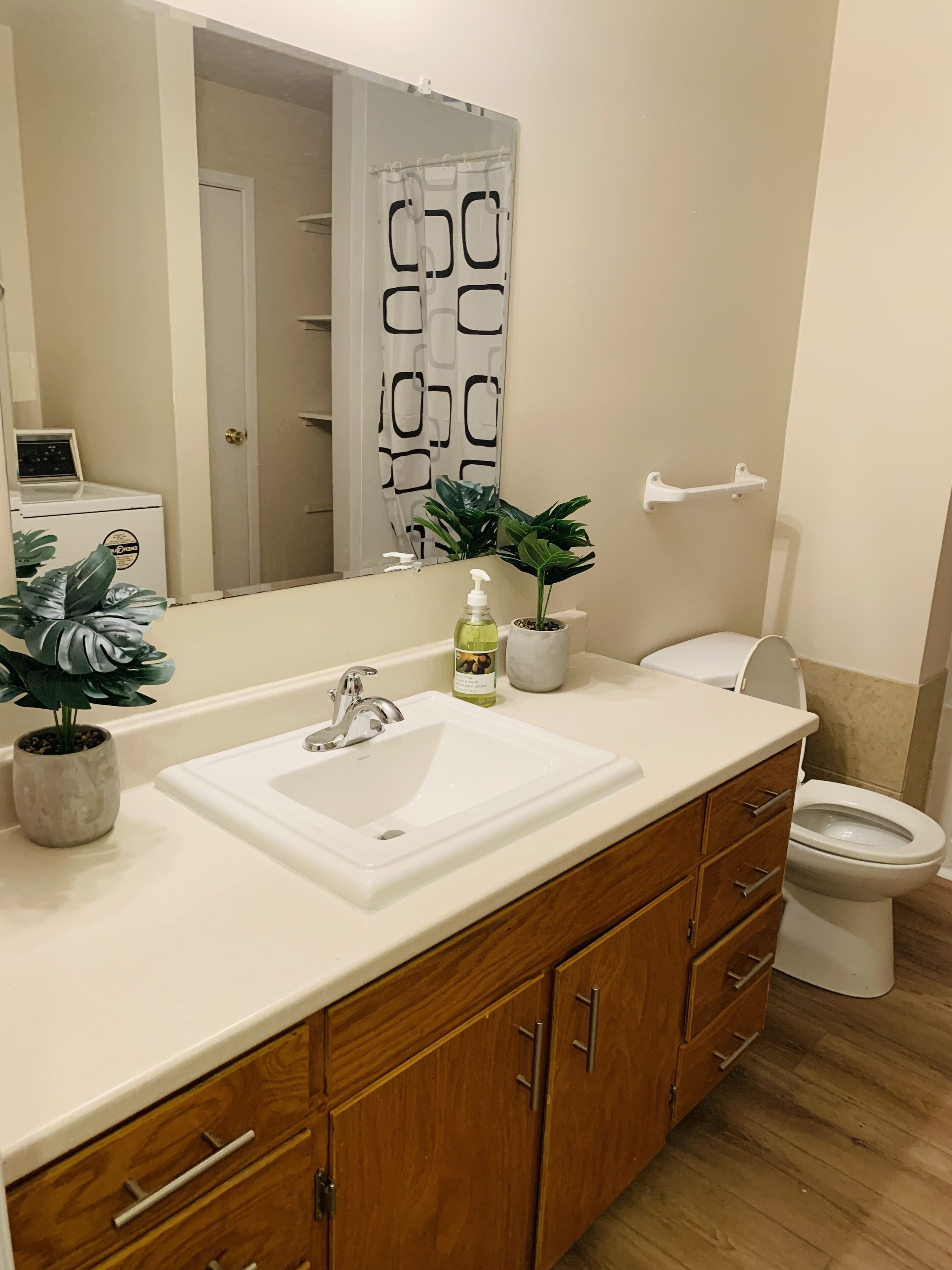 Une salle de bain avec un lavabo blanc, un meuble-lavabo en bois, des toilettes et un rideau de douche à motifs géométriques.