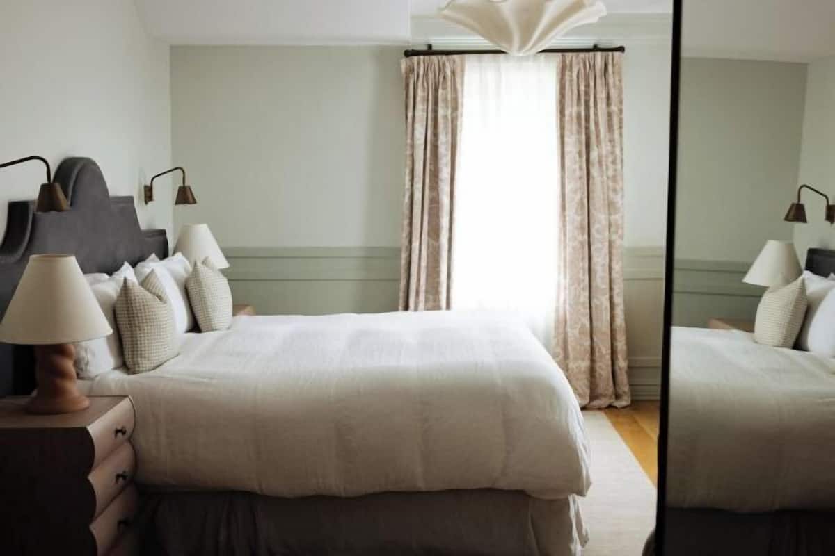 A neatly arranged bedroom with a bed, bedside lamps, a dresser, and a mirror.