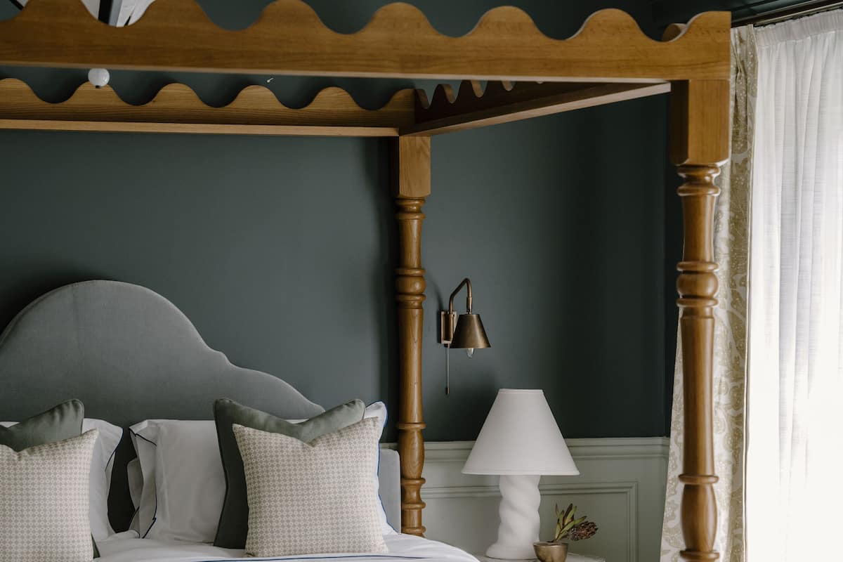 A bedroom with a four-poster bed, a bedside table with a lamp, and a striped sofa.