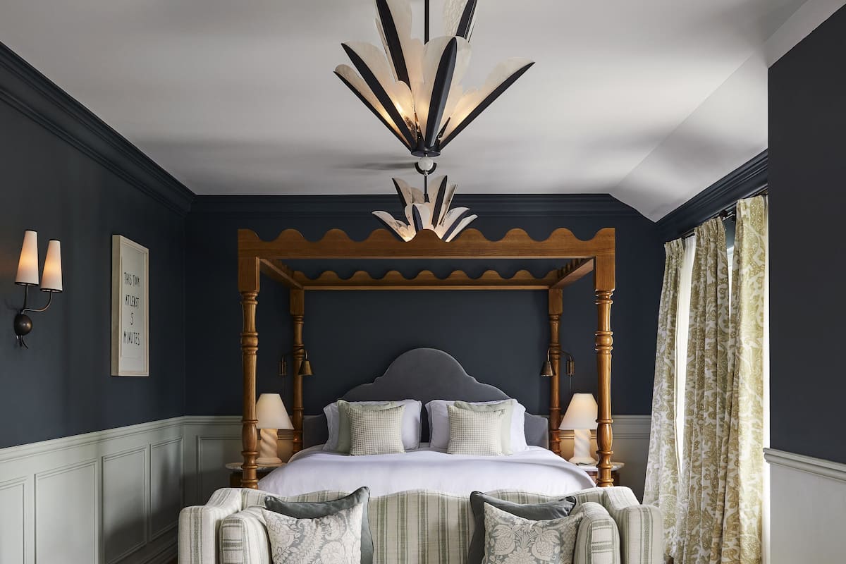 A bedroom with a four-poster bed, a round coffee table, two armchairs, and a chandelier.