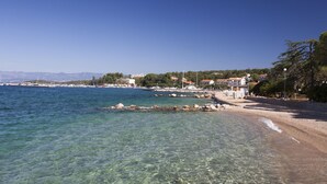 A coastal view with clear water, a sandy beach, and buildings in the background. - Sunny Apt Malinska Krk 800m From Sea (Malinska-Dubasnica)