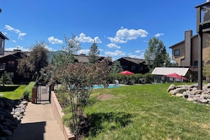 A residential area with a swimming pool, a red umbrella, and a stone pathway leading to a gated entrance.