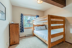 A bunk bed room with a window, a wooden cabinet, and a ceiling light fixture.