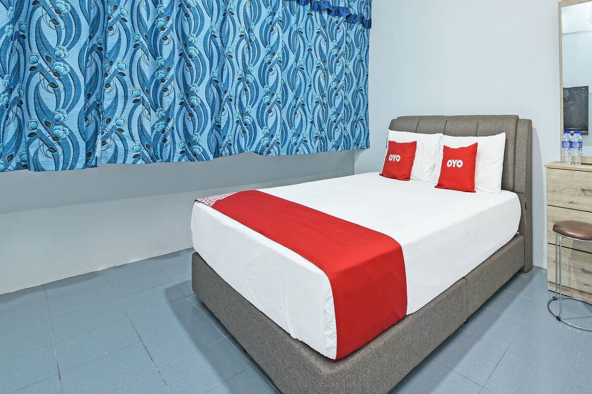 Ein modernes Schlafzimmer mit einem grau gepolsterten Bett, weißer und roter Bettwäsche und blumigem, blauem Wandpapier.