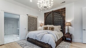 Ein Schlafzimmer mit einem großen Bett, einer Kronleuchter, einem Holzkopfteil und einem Nachttisch mit einer Lampe.
