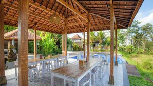 An outdoor covered patio with wooden tables and chairs, a pool, and lush greenery. - Tanta Escape (Sebatu)