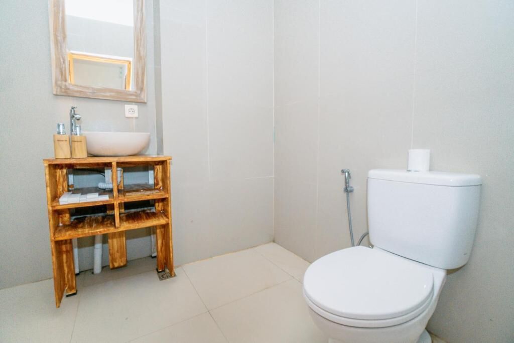 A bathroom with a white toilet, a wooden vanity with a mirror, and a white sink.