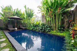 A swimming pool with lounge chairs and an umbrella, surrounded by lush tropical plants.