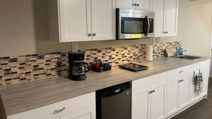 A kitchen with white cabinets, a stainless steel microwave, a coffee maker, and a dishwasher.