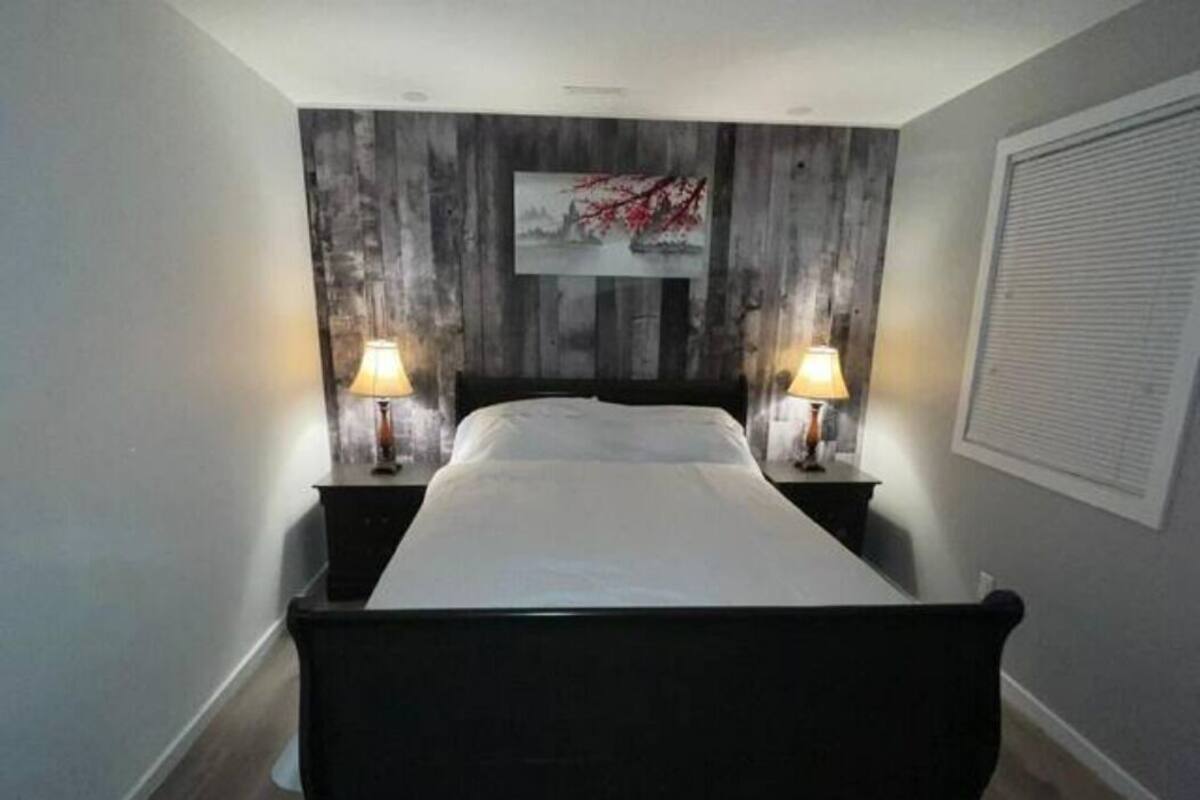 Un dormitorio con una cama, dos lámparas de noche, una obra de arte en la pared y una ventana con persianas.