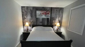 A bedroom with a bed, two bedside tables with lamps, a wall-mounted artwork, and a window with blinds.