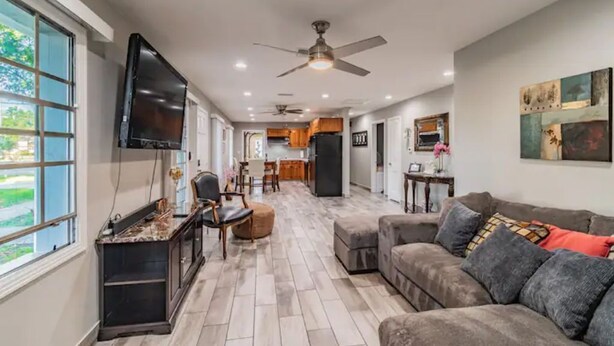 A spacious living area with a large gray sofa, a flat-screen TV mounted on the wall, and a ceiling fan. - Town 'n' Country Cozy Corner: Your Florida Fun Hub (Tampa)