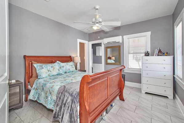 Een slaapkamer met een houten bed, een plafondventilator, een dressoir en een spiegel.