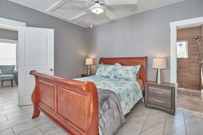 Een slaapkamer met een houten bed, twee nachtkastjes met lampen, een plafondventilator en een douchehoek.