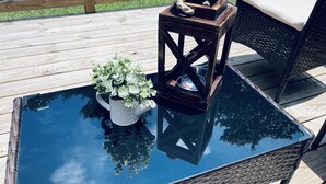 Een glazen tafel met een potplant en een lantaarn op een houten terras.