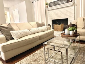 A living room with a beige sofa, a glass coffee table, a fireplace, and a white brick wall. - Entire Home in Conyers (Conyers)
