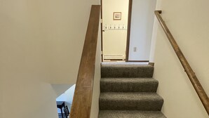 Una escalera alfombrada con barandillas de madera, que lleva a un cuarto con una puerta y un cuadro en la pared.