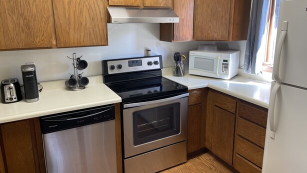 Una cocina compacta con gabinetes de madera, estufa de acero inoxidable, microondas y lavavajillas.