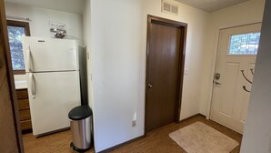 Una cocina compacta con un refrigerador blanco, un cubo de basura de madera y una alfombra color beige.
