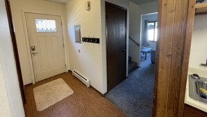 Un pasillo con una puerta blanca, un perchero, un termostato y una escalera que lleva a otra habitación.