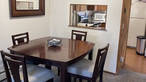 Un comedor con mesa y sillas de madera, una cocina con electrodomésticos y un espejo en la pared.