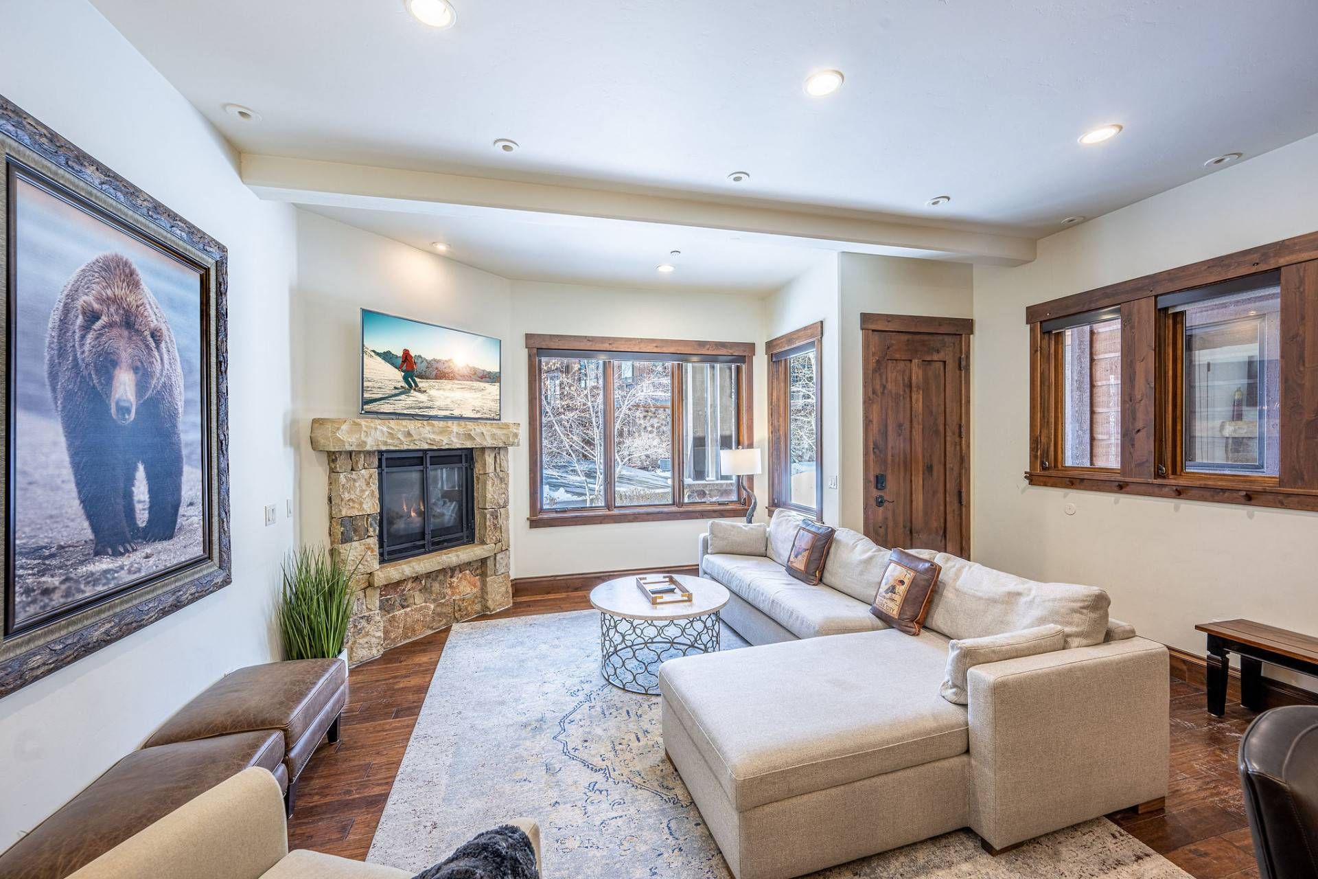 A spacious living room with a stone fireplace, comfortable seating, and large windows offering views of the outdoors.