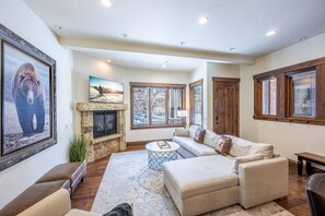 A spacious living room with a stone fireplace, comfortable seating, and large windows offering views of the outdoors.