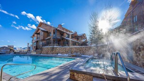 A pool area with a hot tub, stone steps, and a view of a lodge with a stone facade and wooden balconies.