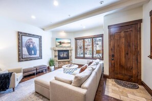 A spacious living room with a fireplace, a large sofa, a coffee table, and a door leading to another room.