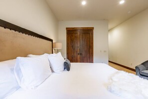 A hotel room with a large bed, a wooden door, and a chair. - Juniper Landing (Park City)